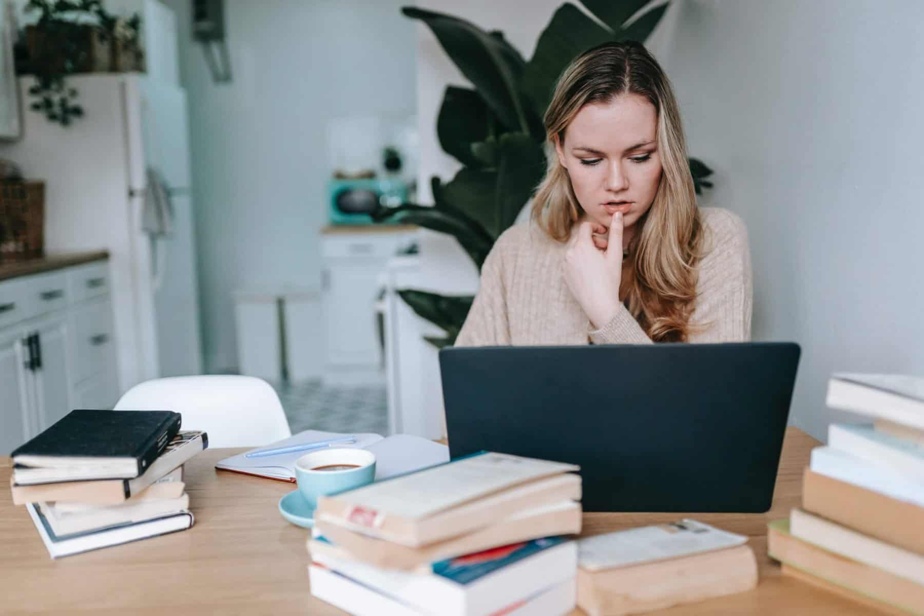 Woman working at laptop surrounded by books