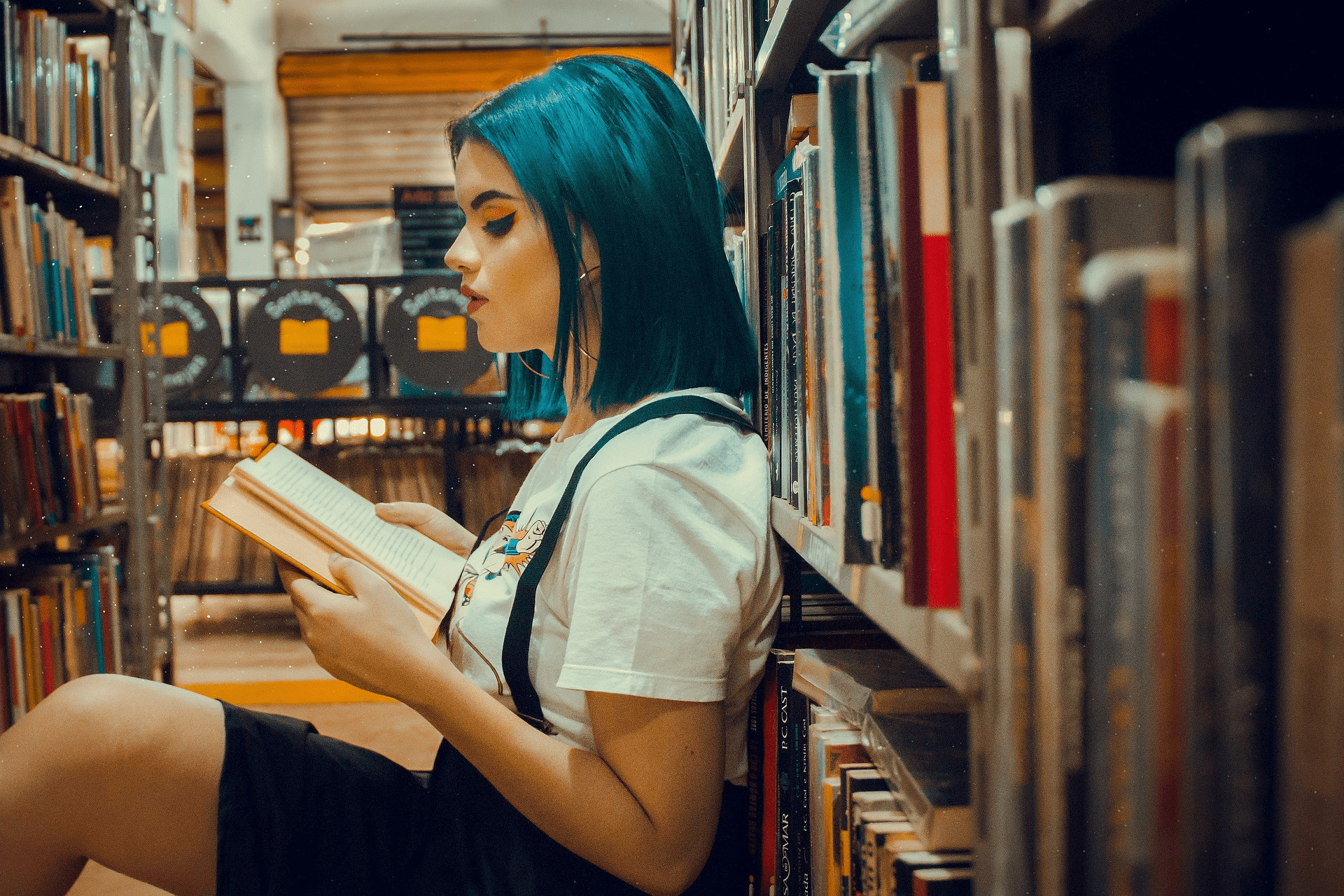 Image of young woman sat on the floor of a library, reading